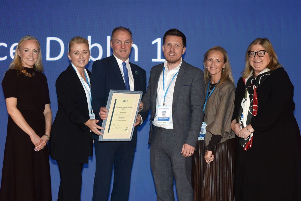 representatives from the award presenting team and recipients pose with award in front of screen