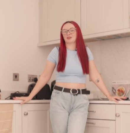 woman with red hair stands in kitchen of her home, leaning into the corner where the counters meet and with appliances in the background