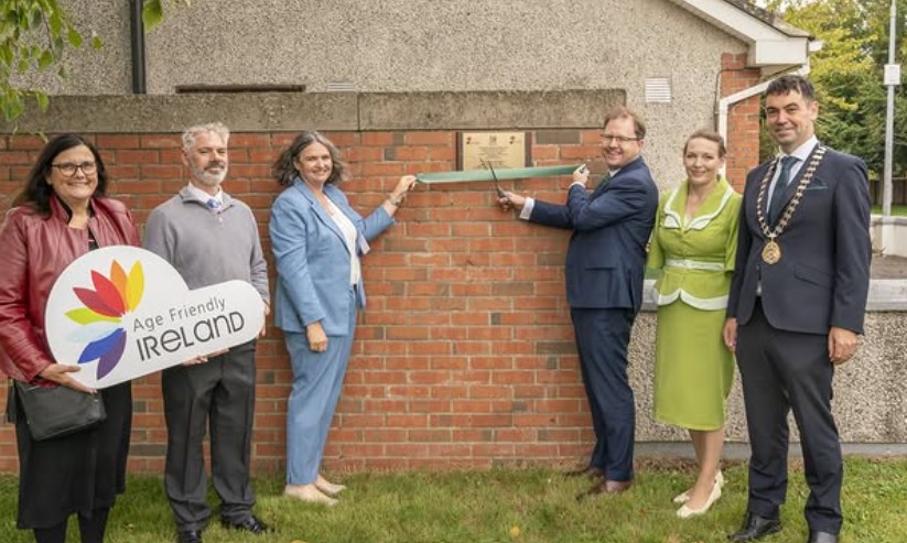 Representatives from Age-Friendly Ireland, Louth County Council and Castelfens stand in front of plaque and wall, cutting ribbon on this age-friendly housing estate
