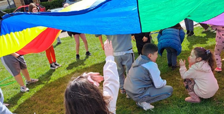 children playing on grass under rainbow-coloured parachute at community event