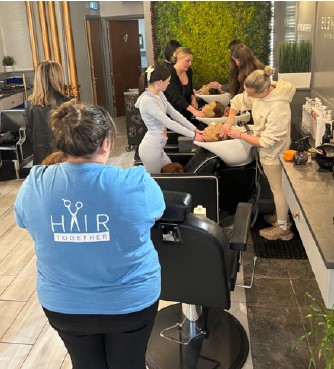 younger Tuath residents take part in HairTogether in a hair salon, washing hair over sinks with a volunteer from HairTogether standing with their back to the camera