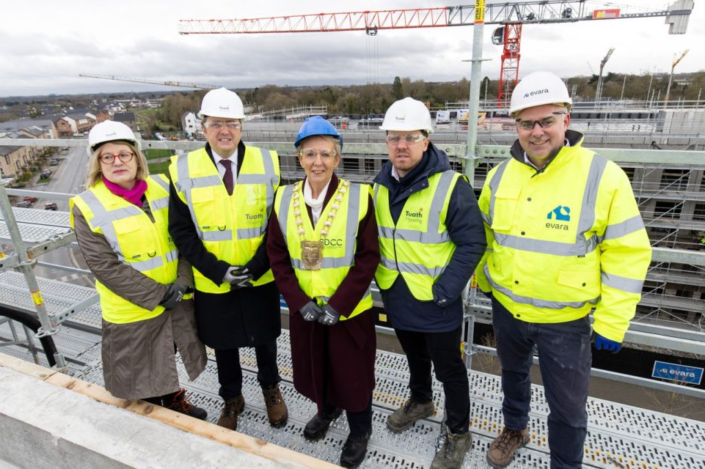 stakeholder partners in hard hats and hivis smile for photo on top of building with construction site and crane in background 