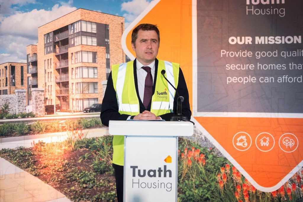 Minister speaks at podium in front of Tuath banner 