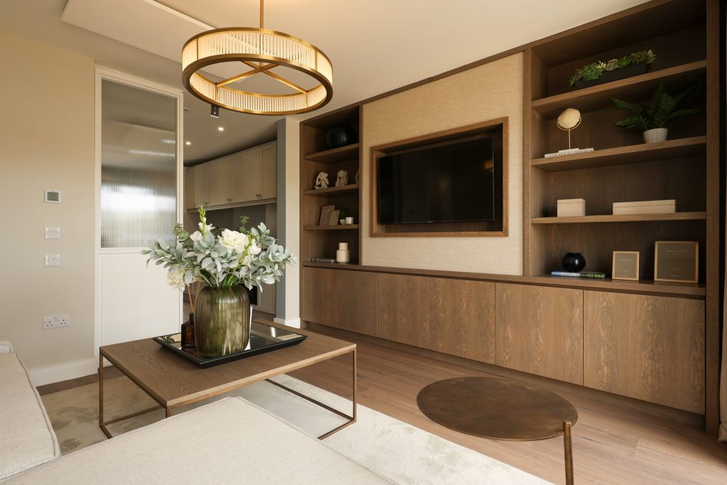 Show home living room at Bennetstown with a fitted timber media wall and shelving, a wall-mounted television and a pendant light.