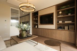 Show home living room at Bennetstown with a fitted timber media wall and shelving, a wall-mounted television and a pendant light.