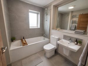 Show home bathroom at Hearthfield with grey wall tiles, a white toilet and wall-hung basin, a mirror and a chrome heated towel rail.