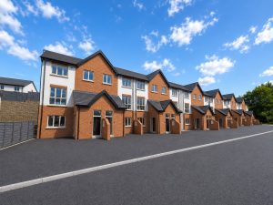 A long row of new three-storey red-brick and white-rendered duplex homes at Hearthfield, with gabled porches over the front doors and a newly surfaced road in front.