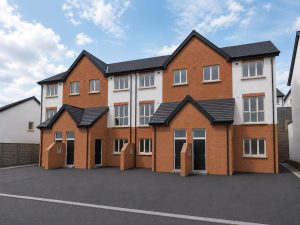 Closer view of a terrace of three-storey duplex homes at Hearthfield in red brick and white render, with grey slate roofs and paired front doors under gabled porches.