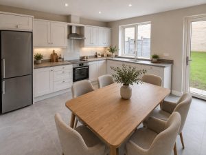 Show home kitchen and dining area at Hearthfield with white shaker-style units, a stainless steel cooker hood and fridge freezer, a timber dining table for six and a door to the garden.